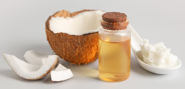 A halved coconut with slices, a small bottle of coconut oil, and a spoon of coconut cream.
